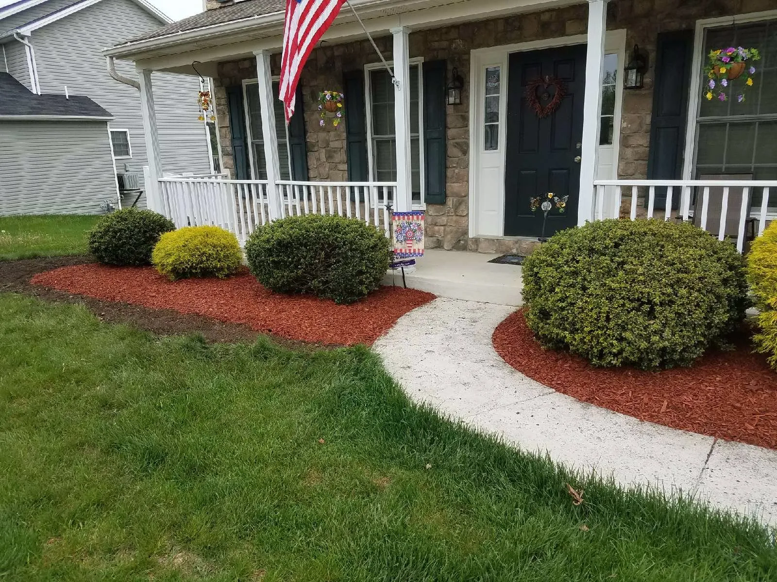 Stone-front home with fresh red-mulch beds, rounded boxwoods and a swept front walkway