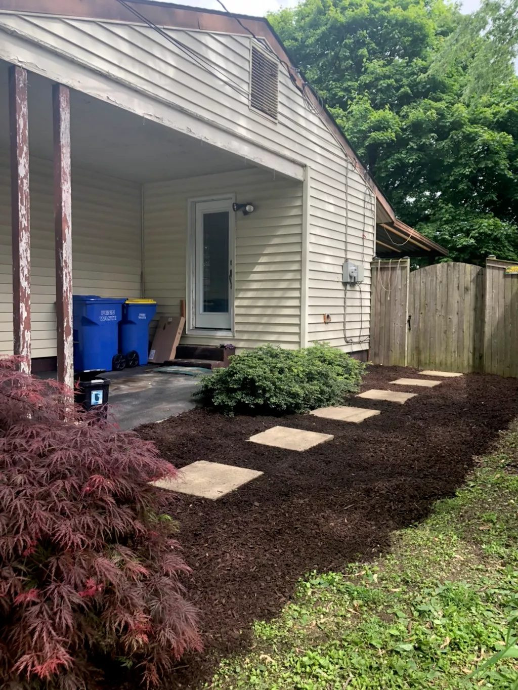 Backyard planting bed with concrete stepping stones, a red Japanese maple and fresh dark mulch
