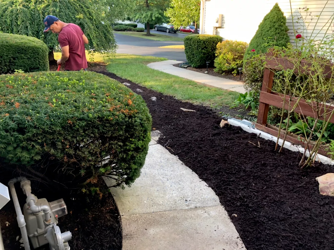 Idalbert Torres in a cap and maroon shirt edging and mulching planting beds along a front walkway