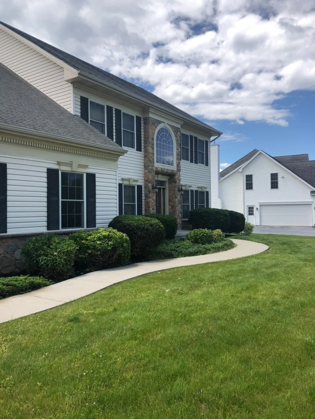 Curved front walkway and neatly trimmed foundation shrubs along a large stone-front colonial